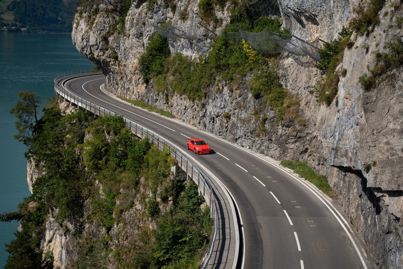 A red sports car on a cliffside road above a lake