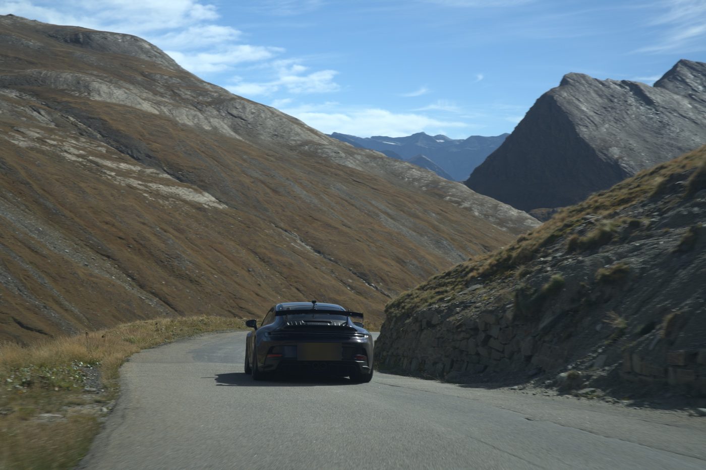 A dark sports car heading into a high Alpine valley