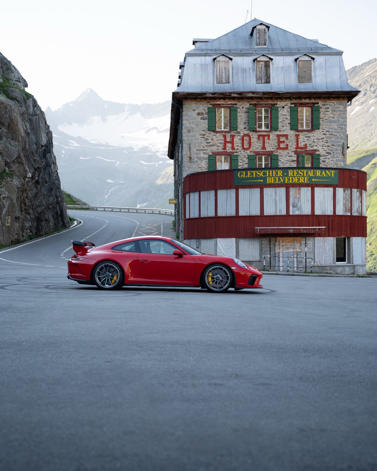A red sports car parked on a hairpin beside an old stone hotel high on an Alpine pass