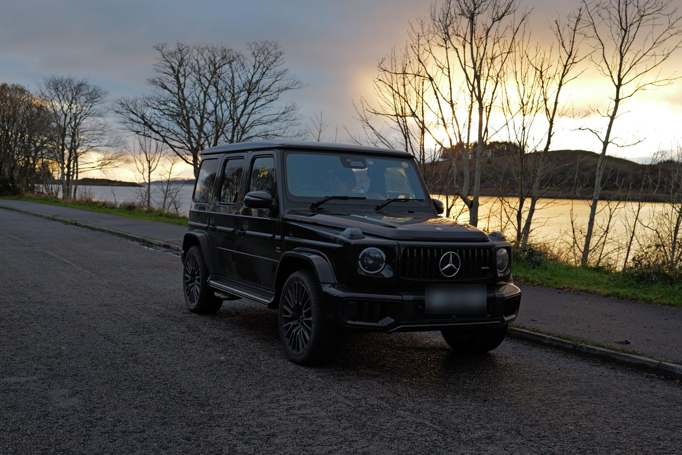 A black SUV on a lakeside road at sunset
