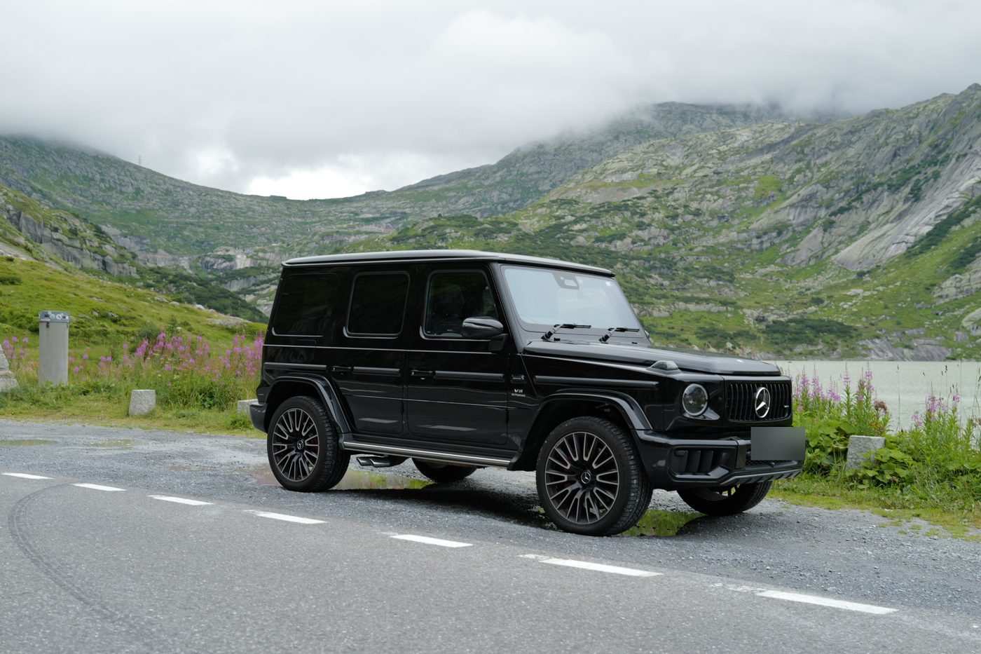 A black SUV beside a mountain lake and wildflowers